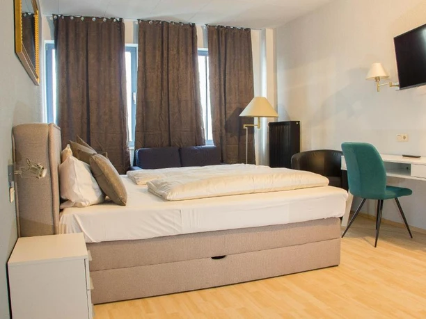 Hotelzimmer im Stargaze Forum Hotel in Hilden Helles Hotelzimmer mit Doppelbett, Schreibtisch, Stuhl, Wand-TV und großzügigen Fenstern mit Vorhängen.