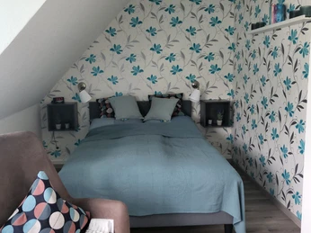 Schlafzimmer in der Ferienwohnung Das Fischerhaus in Velbert. Ein modern eingerichtetes Schlafzimmer unter Dachschrägen mit einem Doppelbett und floraler Tapete.
