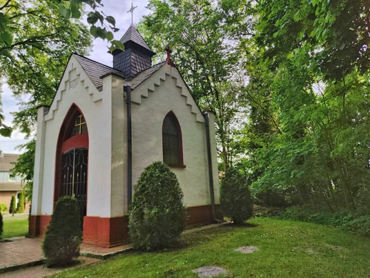 Bredemeiers Kapelle in Hövelhof, umgeben von Bäumen, mit spitzem Dach und dekorativen Fenstern.