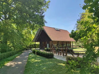 Das Ems-Infozentrum Hövelhof zeigt ein Holzgebäude mit rotem Dach, umgeben von Bäumen und Wiesen.