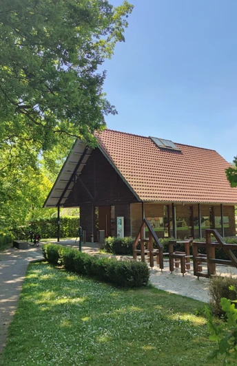 Ems-Infozentrum Hövelhof Das Ems-Infozentrum Hövelhof zeigt ein Holzgebäude mit rotem Dach, umgeben von Bäumen und Wiesen.