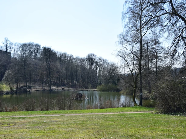 Heilteich Ein idyllischer See mit Uferweg, umgeben von kahlen Bäumen unter klarem Himmel.