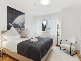 WohnLiebe_Luisenstrasse2.jpeg Helles Schlafzimmer mit großem Fenster, Doppelbett, moderner Dekoration und stilvollen Leuchten.