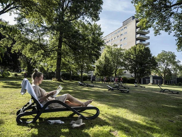 Frau liest auf einer Liege im Park vor dem Gebäude der Salzetalklinik.