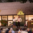 Open-Air-Theateraufführung vor einem Fachwerkhaus, Publikum sieht zwei Schauspielern in Kostümen zu.