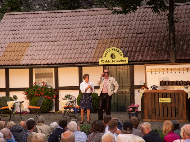 Open-Air-Theateraufführung vor einem Fachwerkhaus, Publikum sieht zwei Schauspielern in Kostümen zu.