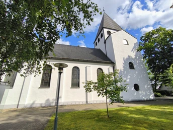 Die Herz-Jesu-Kirche in Hövelriege, weiß getüncht, mit Glockenturm und umliegenden Grünflächen.
