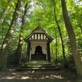 Kapelle am Oberramselhof Eine kleine, weiße Kapelle mit Fachwerkelementen, umgeben von dichtem, grünem Wald.