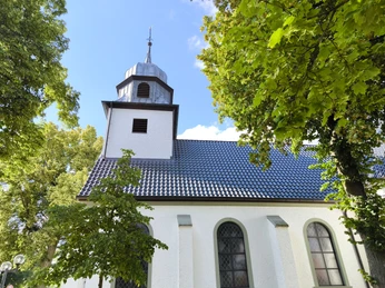 Herz-Jesu-Kirche Espeln Herz-Jesu-Kirche Espeln in Hövelhof, umgeben von grünen Laubbäumen unter klarem, blauem Himmel.