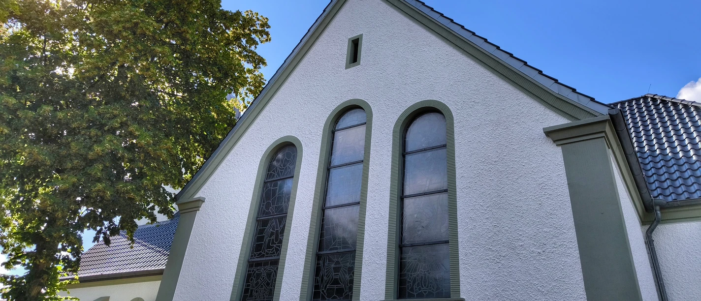 Herz-Jesu-Kirche Espeln Herz-Jesu-Kirche Espeln vor blauem Himmel mit Sonne zwischen belaubten Bäumen, weiße Fassade.