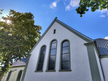 Herz-Jesu-Kirche Espeln Herz-Jesu-Kirche Espeln vor blauem Himmel mit Sonne zwischen belaubten Bäumen, weiße Fassade.