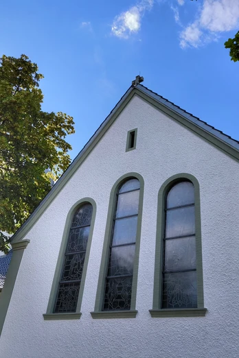 Herz-Jesu-Kirche Espeln Herz-Jesu-Kirche Espeln vor blauem Himmel mit Sonne zwischen belaubten Bäumen, weiße Fassade.