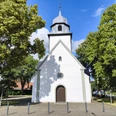 Herz-Jesu-Kirche Espeln Weiße Kirche mit Holztür und Zwiebelturm, umrahmt von Bäumen und blauem Himmel.