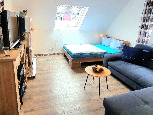 Ferienwohnung Frankes City Sleep in Velbert Wohnraum mit Dachschräge, TV, Sofa und kleinem Tisch in Velberts Frankes City Sleep Ferienwohnung.