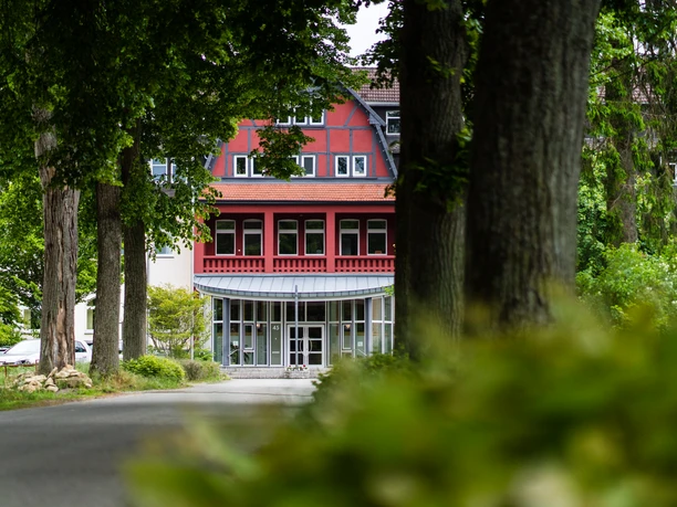 Salvator Kolleg Hövelhof Rotes Gebäude mit Fachwerk und Glasfront in Hövelhof, umgeben von großen Bäumen und grüner Natur.