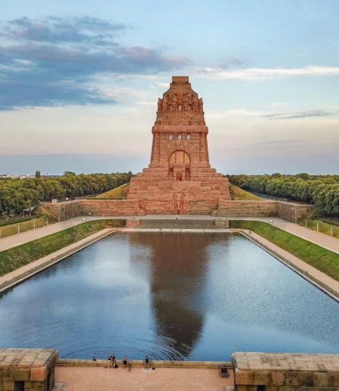voelkerschlachtdenkmal-geschichte-architektur-sehenswuerdigkeiten-back-packer-org-leipzig-travel-800x518.jpg Völkerschlachtdenkmal in Leipzig, frontal fotografiert, mit reflektierendem Wasserbecken davor.