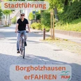 Stadtführung Rädel.jpg Ein Mann fährt bei Sonnenschein auf einem blauen Fahrrad eine schattige Kopfsteinpflasterstraße entlang.