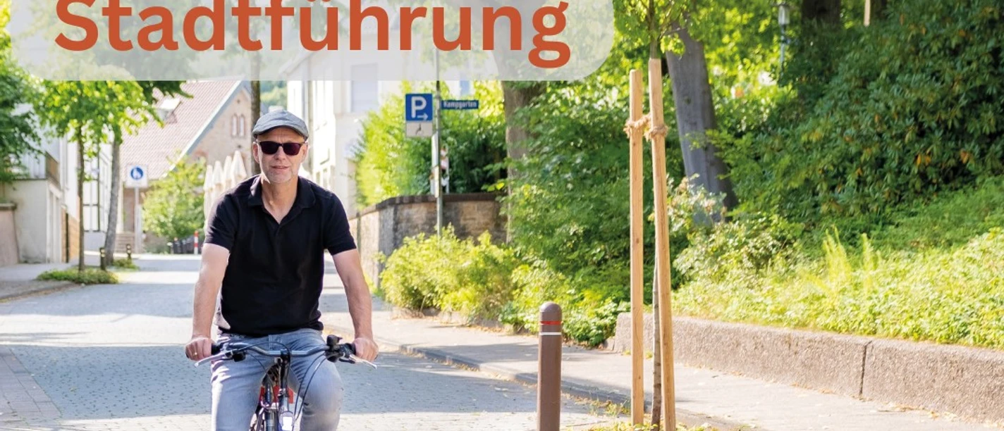 Stadtführung Rädel.jpg Ein Mann fährt bei Sonnenschein auf einem blauen Fahrrad eine schattige Kopfsteinpflasterstraße entlang.