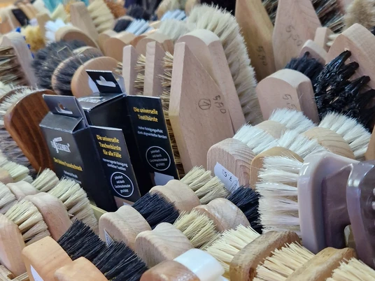 Eine Nahaufnahme handgefertigter Bürsten in verschiedenen Formen und Farben auf einem Marktstand.