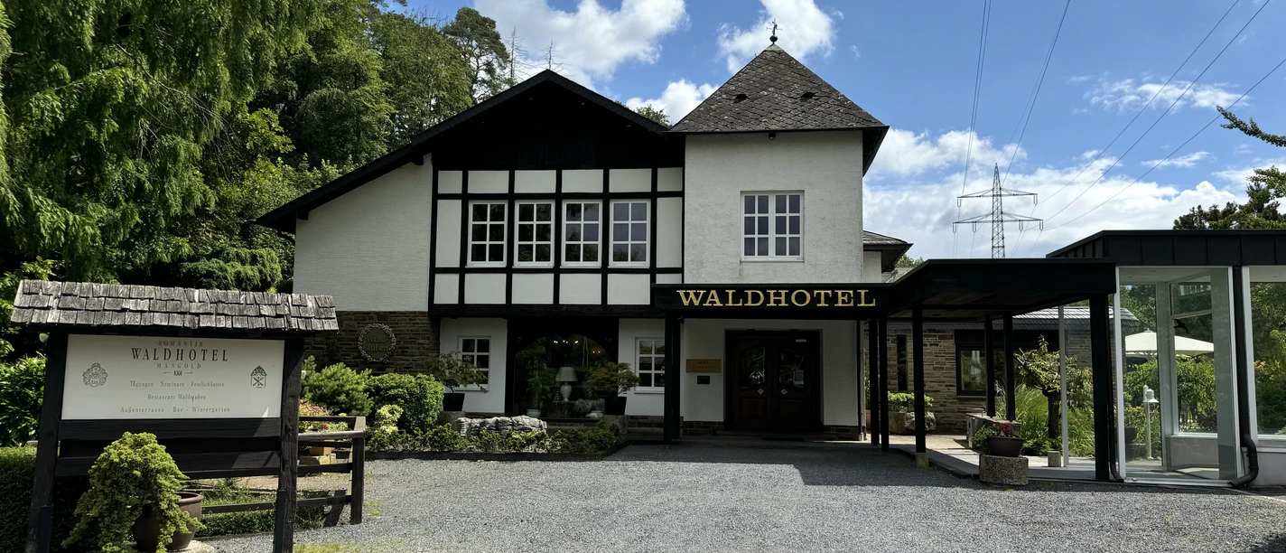 Fachwerkhaus in idyllischer Waldlage, mit großem Eingang und Hotelname gut lesbar, umgeben von Natur.