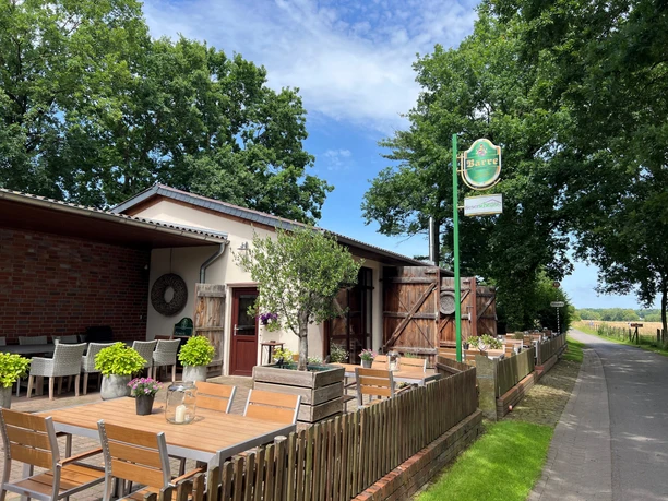 Café Weserscheune Café Weserscheune mit Holzterrasse, hölzernen Gartenmöbeln und grünem Gartenzubehör an einem Sommertag.