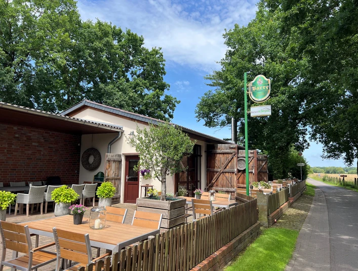 Café Weserscheune Café Weserscheune mit Holzterrasse, hölzernen Gartenmöbeln und grünem Gartenzubehör an einem Sommertag.