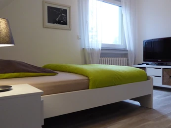 Zimmer in der Panorma Ferienwohnung am neuen Haus Ein modernes Zimmer mit Doppelbett, Flachbildfernseher, Nachttischlampe und großen Fenster.