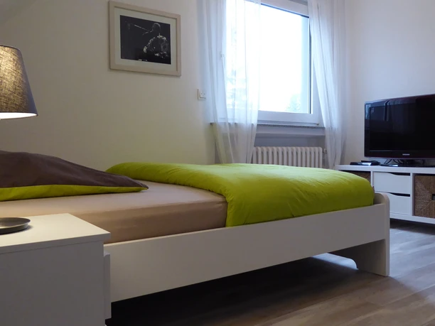 Zimmer in der Panorma Ferienwohnung am neuen Haus Ein modernes Zimmer mit Doppelbett, Flachbildfernseher, Nachttischlampe und großen Fenster.