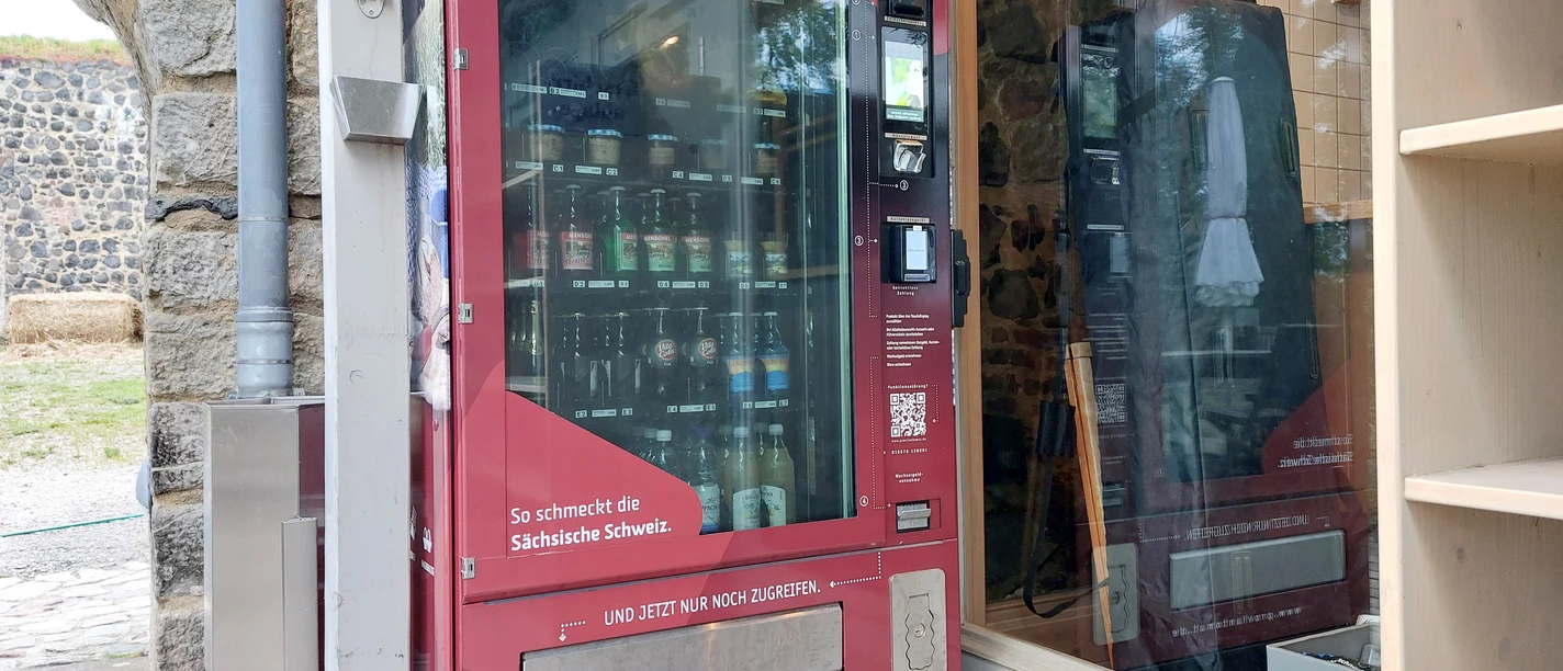 Red vending machine with snacks and drinks, set up next to a stone wall and a wooden shelf.