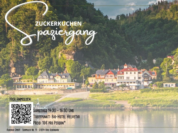 Zuckerkuchen-Spaziergang Eine malerische Flusslandschaft mit Gebäuden im Vordergrund, umgeben von grünen, bewaldeten Hügeln.