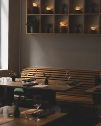 Gedeckter Tisch mit Sitzbank an der Wand und einem Regal darüber, in dem Topfpflanzen und Lichter stehen.