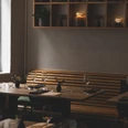 Gedeckter Tisch mit Sitzbank an der Wand und einem Regal darüber, in dem Topfpflanzen und Lichter stehen.