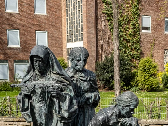 Edith Stein memorial Das Edith-Stein-Denkmal zeigt drei bronzene Frauenfiguren in feierlichen Posen, umgeben von einem gepflasterten Platz und Grünflächen.The Edith Stein monument shows three bronze female figures in solemn poses, surrounded by a paved square and green areas.