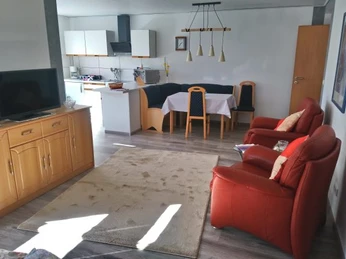 Appartment im Haus Panorama in Ratingen Helles Wohnzimmer mit rotem Sessel, Holzmöbeln, Esstisch und Küchenzeile in moderner Wohnung.