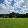 Sportplatz Gristede.jpg Weitläufiger, grün gehaltener Fußballplatz unter blauem Himmel mit Wolken, umgeben von Bäumen.