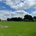 Sportplatz Metjendorf.jpg Ein weitläufiger, grüner Sportplatz in Metjendorf unter einem teils bewölkten Himmel. Im Hintergrund sind Bäume und vereinzelt Gebäude sichtbar.