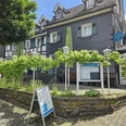 Hauderei Café & Bistro Historisches Fachwerkgebäude mit Außenterrasse, umgeben von Weinreben und Infotafeln unter blauem Himmel.