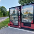 Proviantomat in Ostrau Roter Verkaufsautomat mit Snacks und Getränken, aufgestellt neben einer Landstraße, umgeben von grünen Bäumen und Wiese unter blauem Himmel.Red vending machine with snacks and drinks, set up next to a country road, surrounded by green trees and meadows under a blue sky.Červený automat s občerstvením a nápoji, postavený u venkovské silnice, obklopený zelenými stromy a loukami pod modrou oblohou.Czerwony automat z przekąskami i napojami, ustawiony przy wiejskiej drodze, otoczony zielonymi drzewami i łąkami pod błękitnym niebem.Rode automaat met snacks en drankjes, opgesteld naast een landweggetje, omringd door groene bomen en weiden onder een blauwe hemel.Distributore automatico rosso di snack e bevande, allestito accanto a una strada di campagna, circondato da alberi e prati verdi sotto un cielo azzurro.