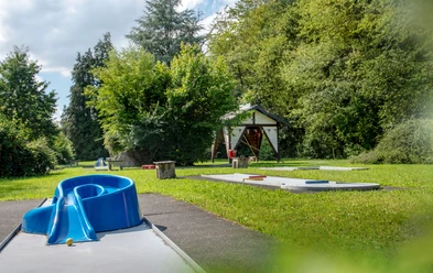 Minigolfanlage in Reichshof-Eckenhagen Minigolfplatz mit blauer Hindernisspirale, umgeben von grünen Bäumen und Wiese, unter blauem Himmel.