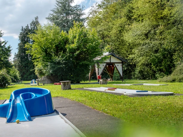 Minigolfanlage in Reichshof-Eckenhagen Minigolfplatz mit blauer Hindernisspirale, umgeben von grünen Bäumen und Wiese, unter blauem Himmel.