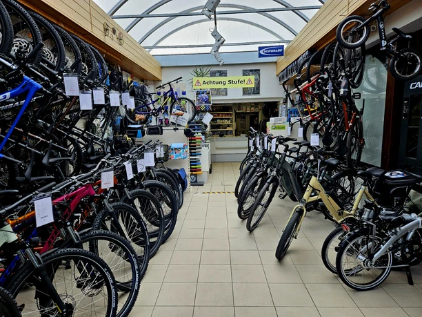 Verkaufsraum mit hochwertigen Fahrrädern Fahrradgeschäft mit zahlreichen Fahrrädern in verschiedenen Farben und Größen, aufgereiht entlang der Wände; Schild "Achtung Stufe!" im Hintergrund.