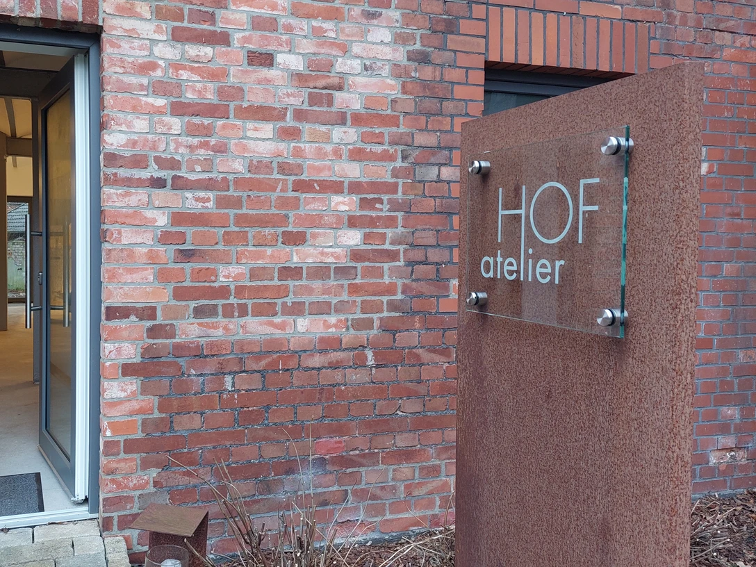 Offene Tür eines Ateliers in einem Backsteingebäude, mit einem modernen Schild "HOF atelier".
