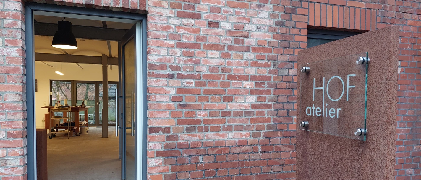 Offene Tür eines Ateliers in einem Backsteingebäude, mit einem modernen Schild "HOF atelier".