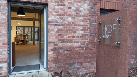 HOF atelier Frille Offene Tür eines Ateliers in einem Backsteingebäude, mit einem modernen Schild "HOF atelier".
