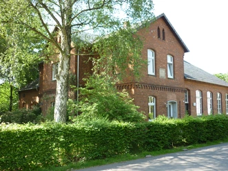 artminden - alte Schule Ehemalige Backsteinschule im Grünen, umgeben von Bäumen und gepflegter Hecke, mit Satteldach.