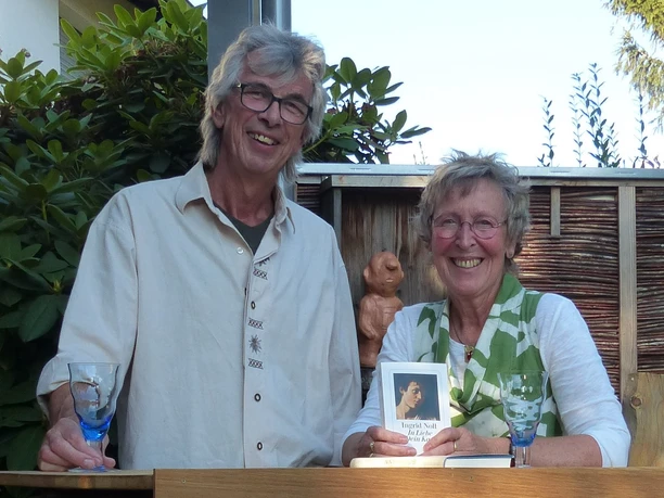 Zwei ältere Personen strahlen in die Kamera, sie stehen lächelnd zusammen, umgeben von Pflanzen.