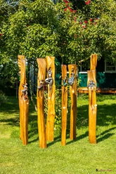 Handwerkermarkt_Christa Staffa.jpg Fünf kunstvoll geschnitzte Holzstämme mit metallischen Verzierungen stehen in einem Garten.