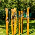 Handwerkermarkt_Christa Staffa.jpg Fünf kunstvoll geschnitzte Holzstämme mit metallischen Verzierungen stehen in einem Garten.
