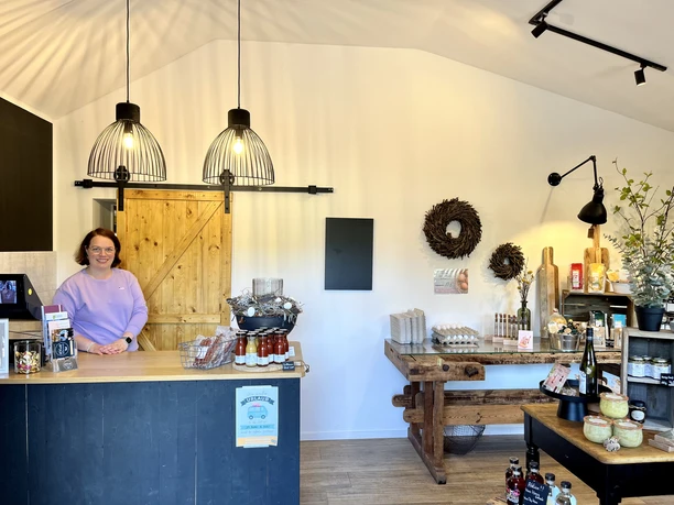 HOF.echt Hofladen Fam. Theissing in Salzbergen ©Emsland Tourismus GmbH (5).jpg Frau hinter Verkaufstresen in modernem Hofladen mit regionalen Produkten und warmem Holzinterieur