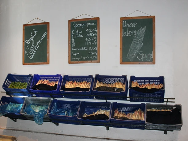 Schroeter & Wielage, Bawinkel - Spargelangebot im Hofladen ©Emsland Tourismus GmbH.JPG Mehrere Kisten mit frischem weißen und grünem Spargel unter Tafeln mit Preisen im Hofladen.